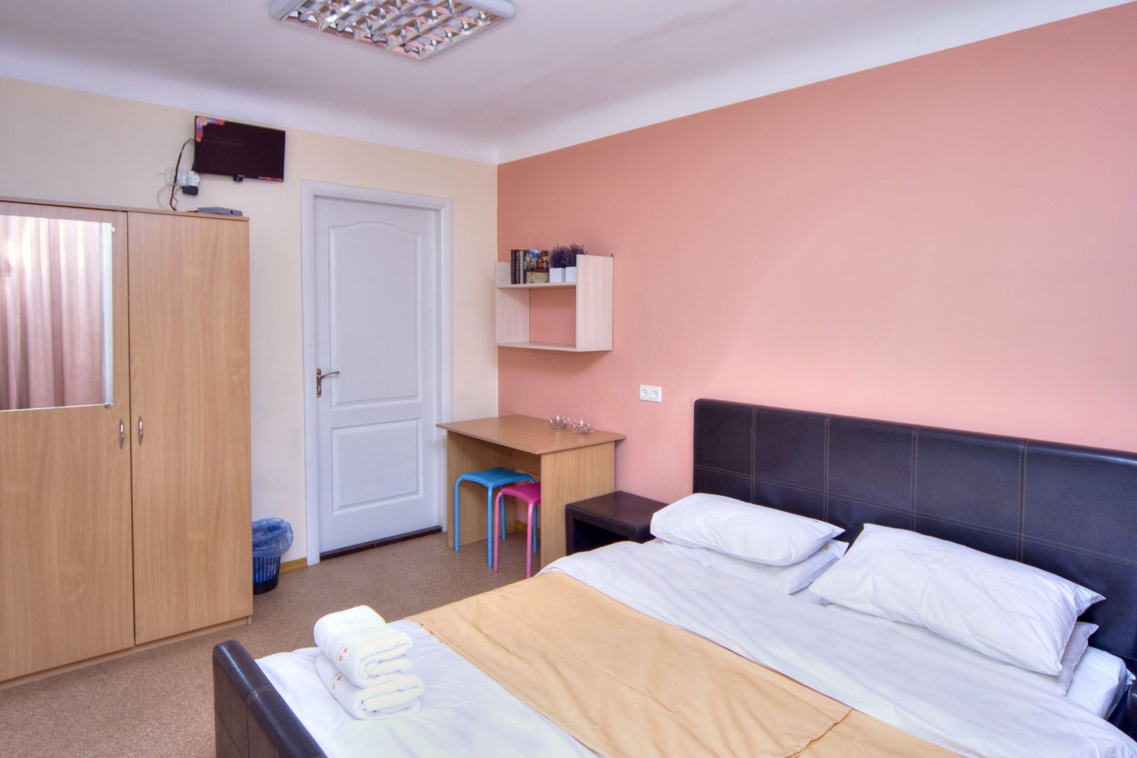 A bedroom with a bed, a desk, a chair, a wardrobe, and a shelf.