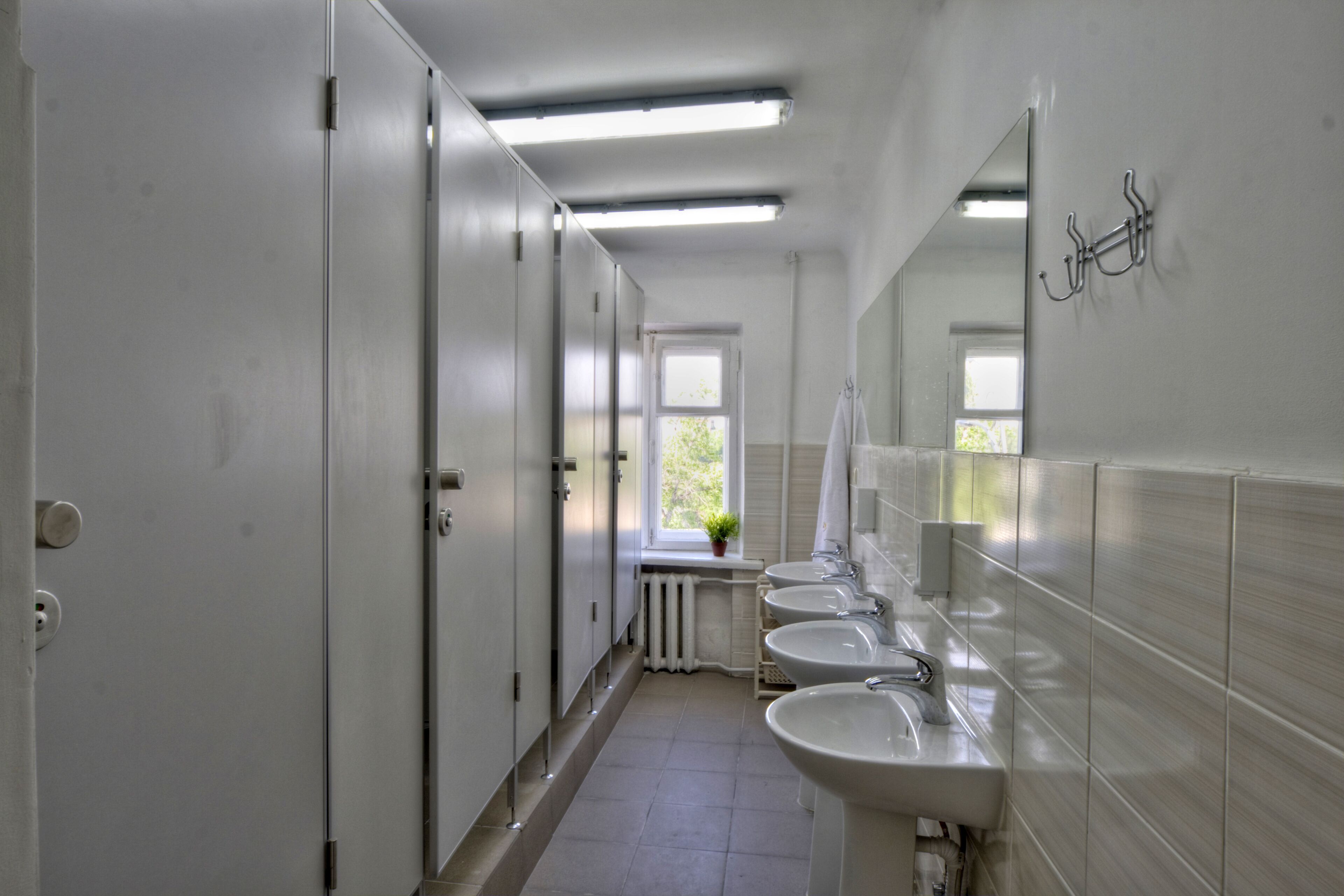 A corridor with three sinks and a mirror on the right wall.