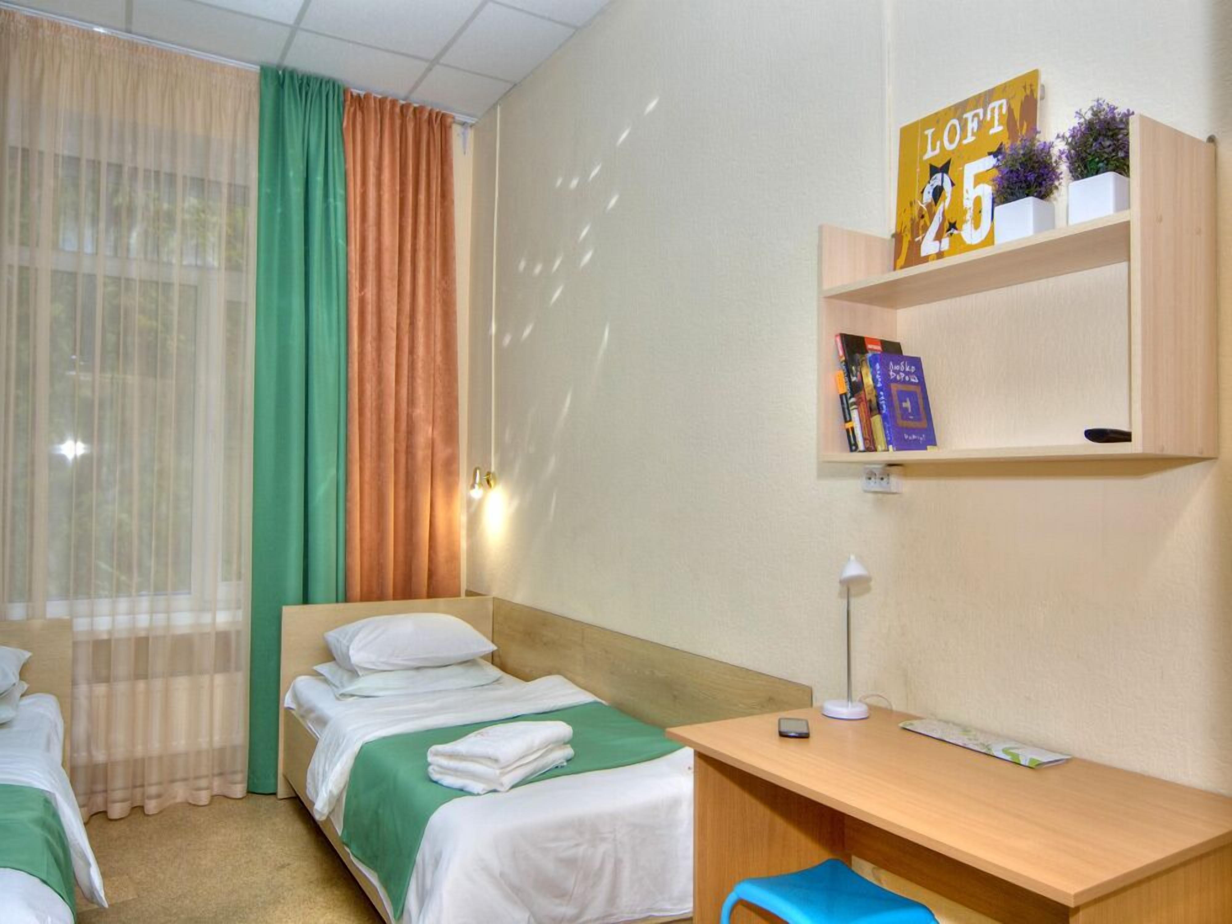 Une chambre d’hôtel avec deux lits, un bureau et une étagère contenant des livres et un panneau.