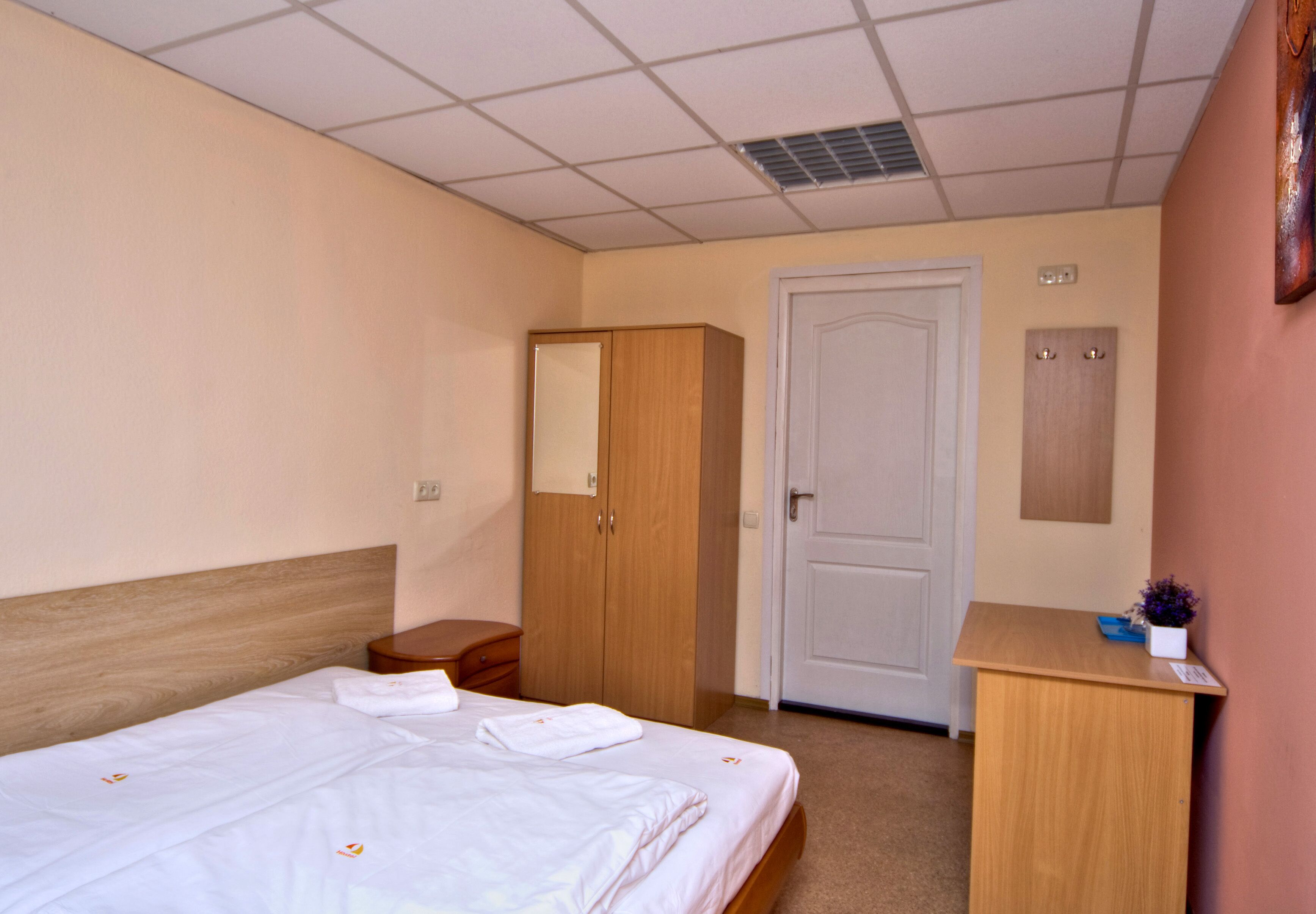 Een hotelkamer met een bed, een houten kledingkast, een bureau en een deur.