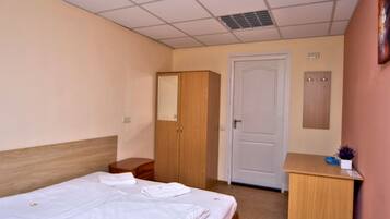 Een hotelkamer met een bed, een houten kledingkast, een bureau en een deur.