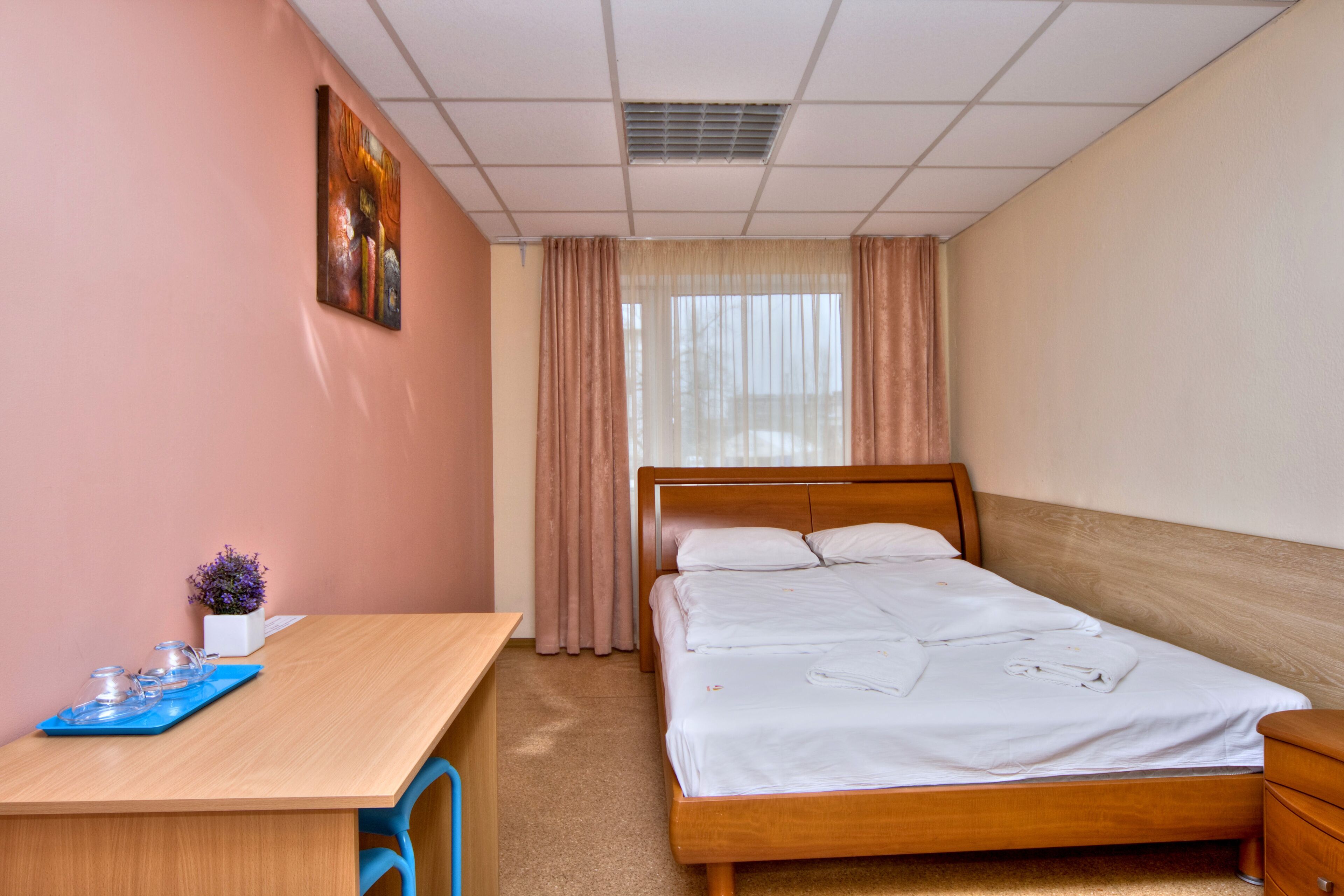 Camera d'albergo con un letto di legno, una scrivania con una sedia, un tavolino con un vaso di fiori e un quadro appeso al muro.