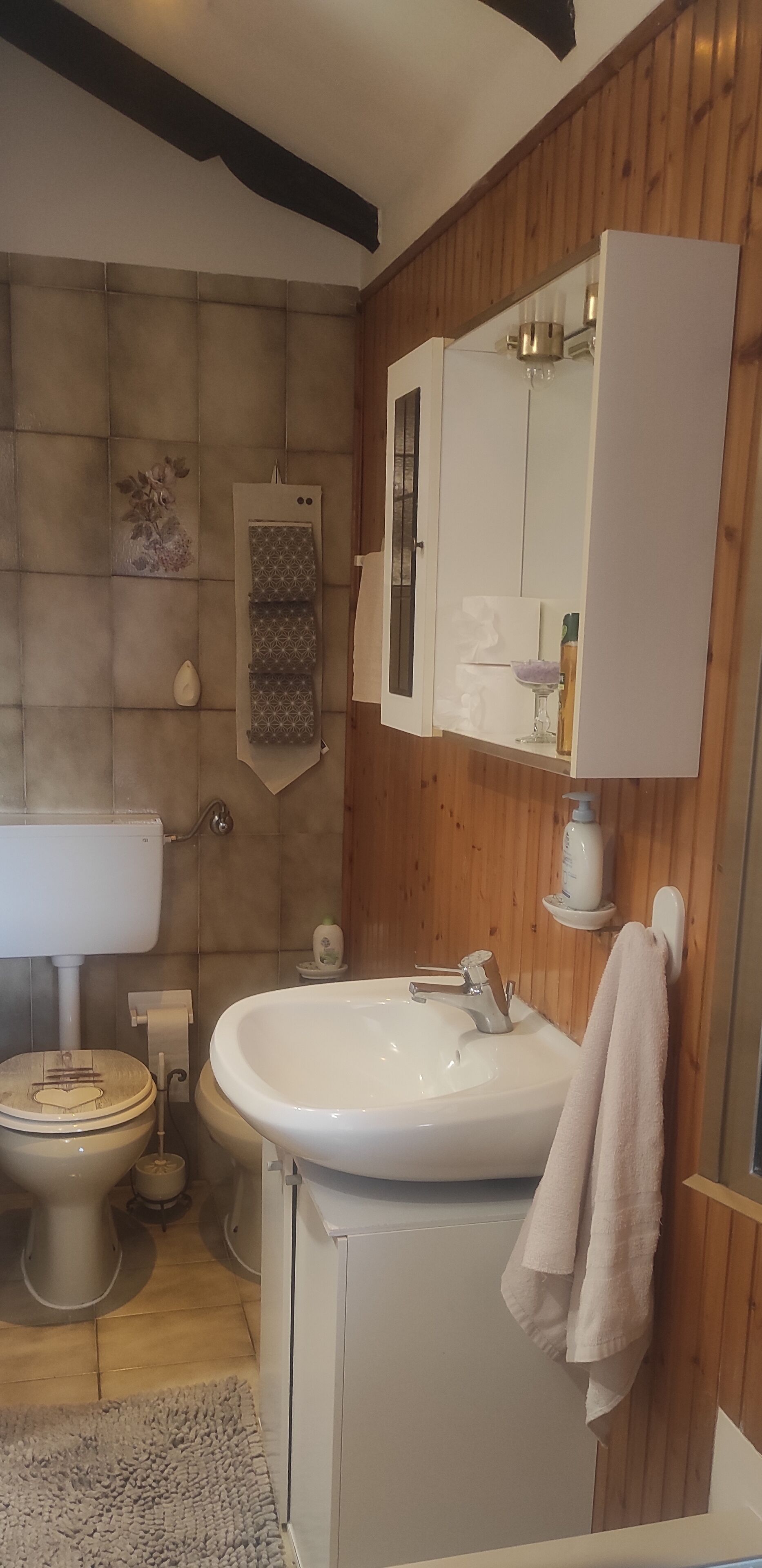 Une salle de bain avec un mur en bois, un lavabo blanc, des toilettes et un meuble avec miroir.
