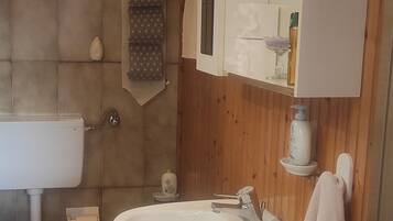 Une salle de bain avec un mur en bois, un lavabo blanc, des toilettes et un meuble avec miroir.