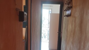 Een gang met betegelde vloer, een metalen rek en een deur naar een lichte kamer.