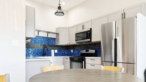 Una cucina moderna con mobili bianchi, zoccolo blu, elettrodomestici in acciaio inossidabile e un tavolo rotondo in legno con sedie.