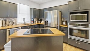 Une cuisine moderne avec des meubles de couleur sombre, des appareils électroménagers en acier inoxydable et un îlot central en bois.