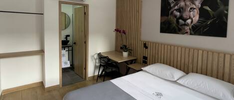 Ein Hotelzimmer mit Bett, Schreibtisch, Stuhl, einer Pendelleuchte, einer Klimaanlage und einem Wandbild.