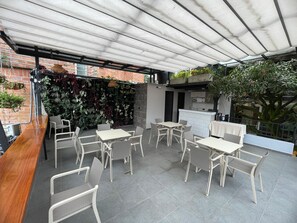An outdoor patio area with a covered seating area, a bar, and a brick wall with plants.