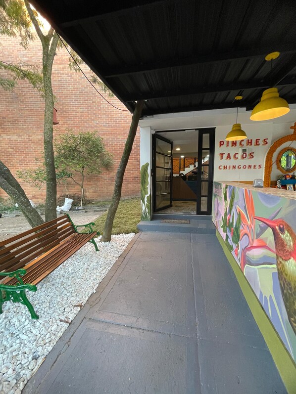 An outdoor seating area with a bench and a pathway leading to a building with a sign reading "PINCHES TACOS CHINGONES".