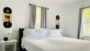 A bedroom with a bed, a nightstand, and wall-mounted record players. - Cozy & Centrally Located APT - KING BED
 (Evansville)