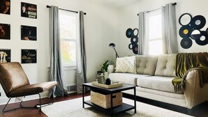 Un salón con sofá, sillón, mesa de centro y decoración en la pared.