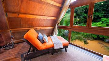 A wooden room with a bed, a window, and a view of the forest.