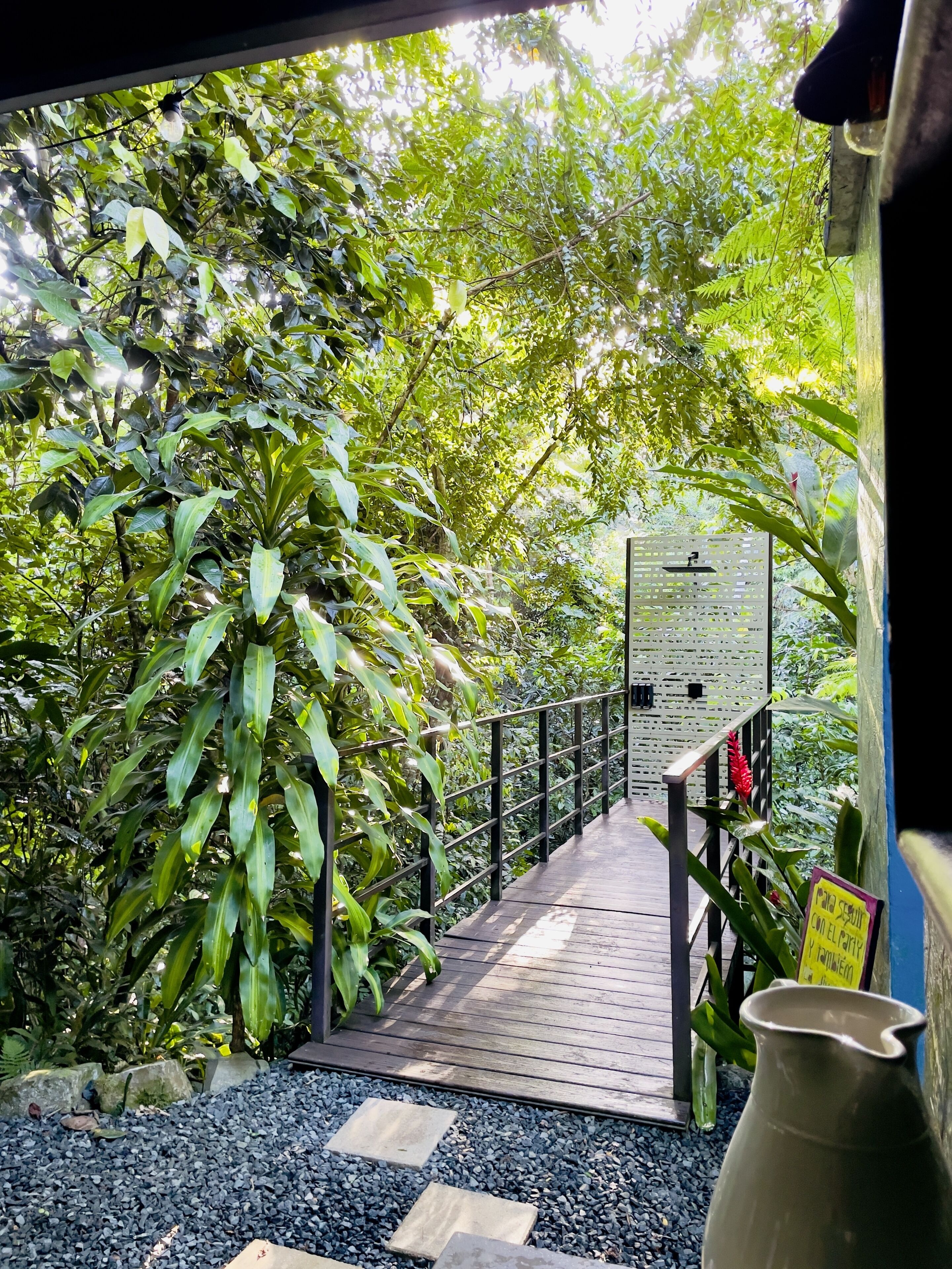 Un sendero de madera que atraviesa un exuberante jardín, con un cartel y un jarrón.