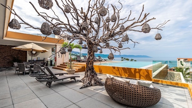 Un salón en la azotea con mobiliario de mimbre, una escultura decorativa de un árbol y vistas al océano.