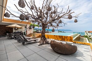 A rooftop lounge with wicker furniture, a decorative tree sculpture, and a view of the ocean.