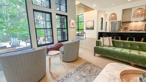 A spacious living room with large windows, a green sofa, and a dining area with chairs and a table. - The Birch Bower: Luxury Lakefront Home (Oakland)