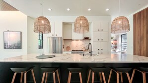 A modern kitchen with a large island, stainless steel appliances, and wooden stools. - The Birch Bower: Luxury Lakefront Home (Oakland)