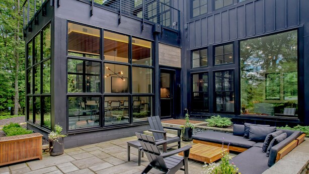 A modern outdoor patio with a wooden bench, a sofa, and a dining table. - The Birch Bower: Luxury Lakefront Home (Oakland)