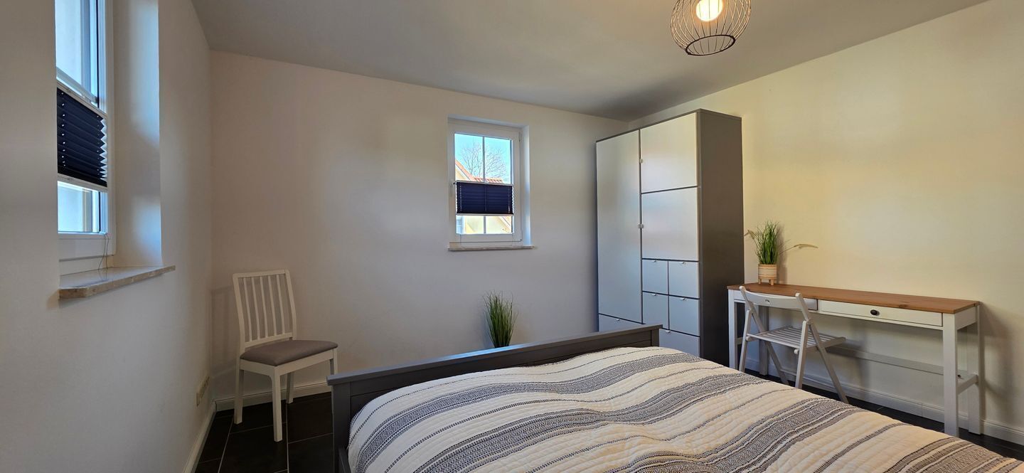 Un dormitorio con cama, escritorio, silla, armario y ventana.