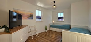 A bedroom with a bed, a TV, a chair, and two windows.