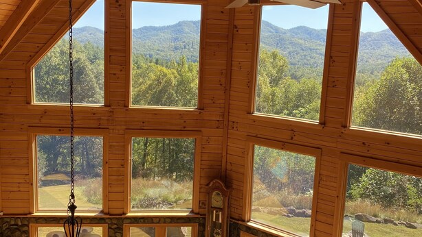 A spacious room with large windows, a ceiling fan, a chandelier, and a stone fireplace. - Dramatic Remodeled Log home with everything! (Franklin)