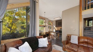A spacious living room with a large window, leather sofas, a wooden coffee table, and a kitchen in the background. - Mountain Retreat Near Hiking and Golf In Silverthorne (Silverthorne)