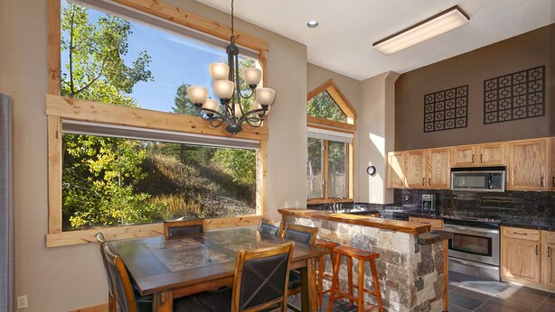 A modern kitchen with a large island, wooden cabinetry, and a view of a forest through large windows. - Mountain Retreat Near Hiking and Golf In Silverthorne (Silverthorne)