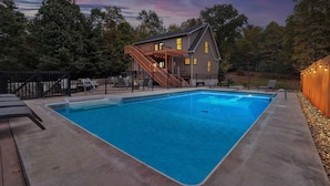 Ein rechteckiger Swimmingpool mit einer Holzterrasse und einem überdachten Außenbereich mit Treppe.