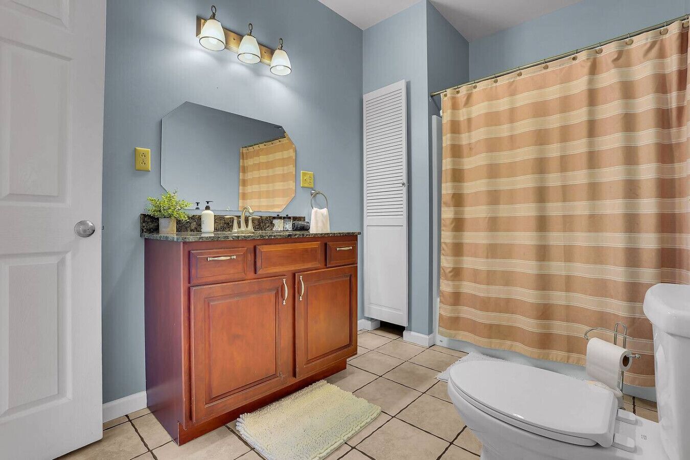 A bathroom with a wooden vanity, a toilet, a striped shower curtain, and a light blue wall.