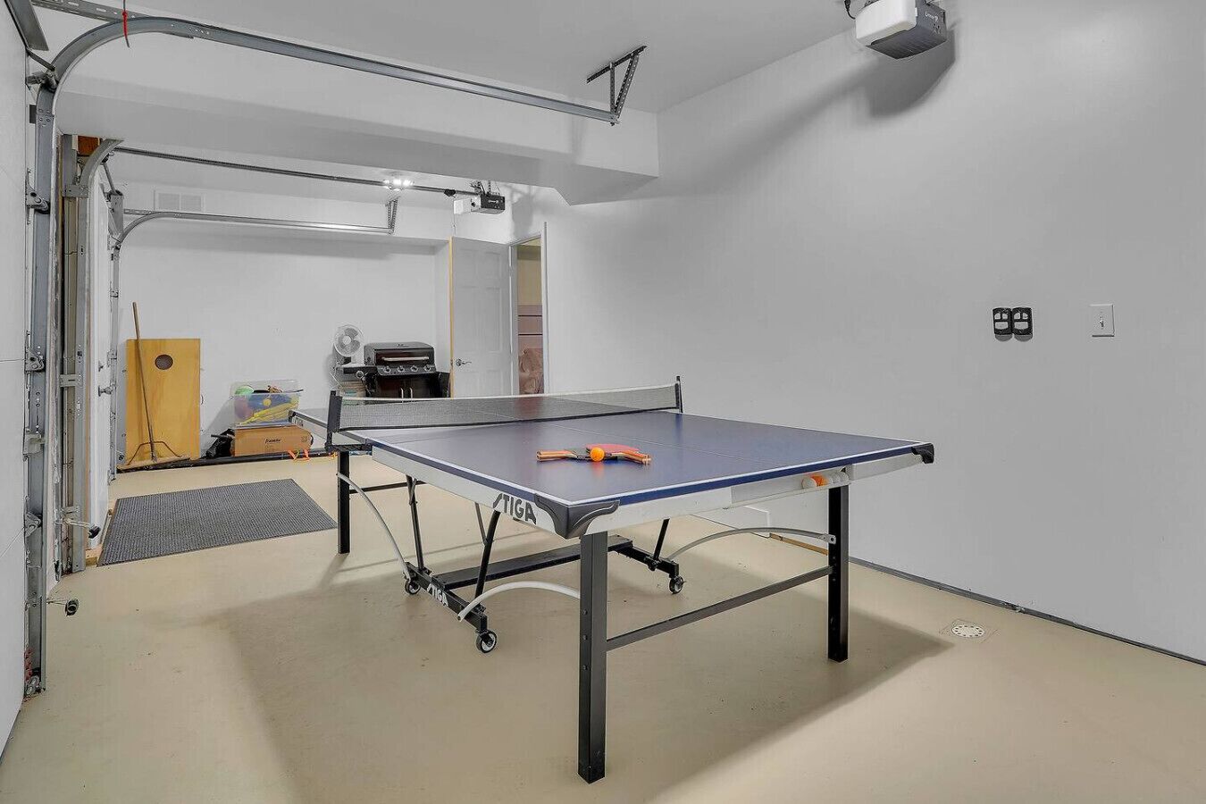 A ping pong table in a room with a white wall and a door leading to another room.