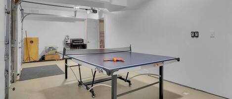 A ping pong table in a room with a white wall and a door leading to another room.