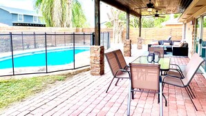 A covered patio with a pool, outdoor furniture, and a view of a house in the background. - Tall Palms Oasis (McAllen)