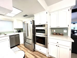 Una cocina moderna con electrodomésticos de acero inoxidable, armarios blancos y piso de madera.