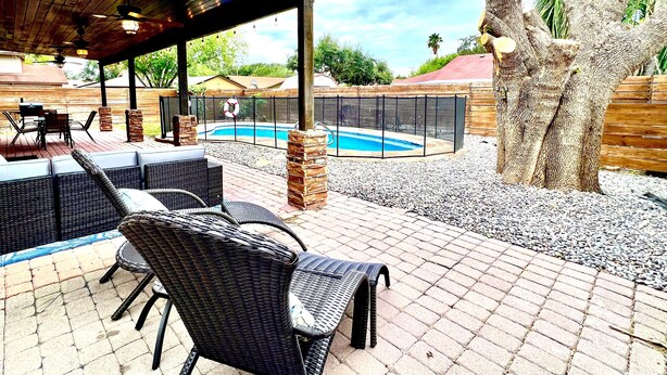 An outdoor patio with wicker furniture, a pool, and a covered area with a ceiling fan. - Tall Palms Oasis (McAllen)