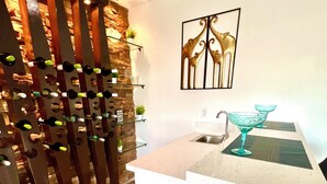 A kitchen with a wooden wine rack, a white countertop, and a bar area with stools. - Tall Palms Oasis (McAllen)