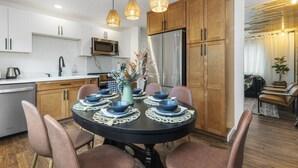 A modern kitchen with white cabinets, a stainless steel refrigerator, and a dining table set with bowls and plates. - Luxury Living-Kirkland: Stylish Home - Prime Spot! (Kirkland)