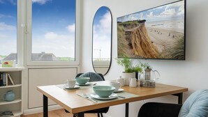 A modern room with a wooden table, chairs, a large mirror, and a framed beach photograph. - Himmelblau - Modern Renovierte, Zentrale Whg. Inkl. Pkw-stellplatz, Wlan. Haustiere Erlaubt (Westerland)