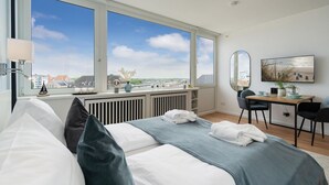 A hotel room with a bed, a desk, and a large window offering a city view. - Himmelblau - Modern Renovierte, Zentrale Whg. Inkl. Pkw-stellplatz, Wlan. Haustiere Erlaubt (Westerland)