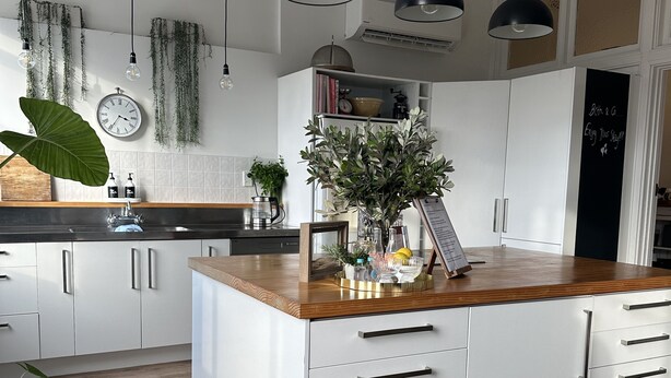 A modern kitchen with white cabinets, a wooden countertop, and pendant lighting.