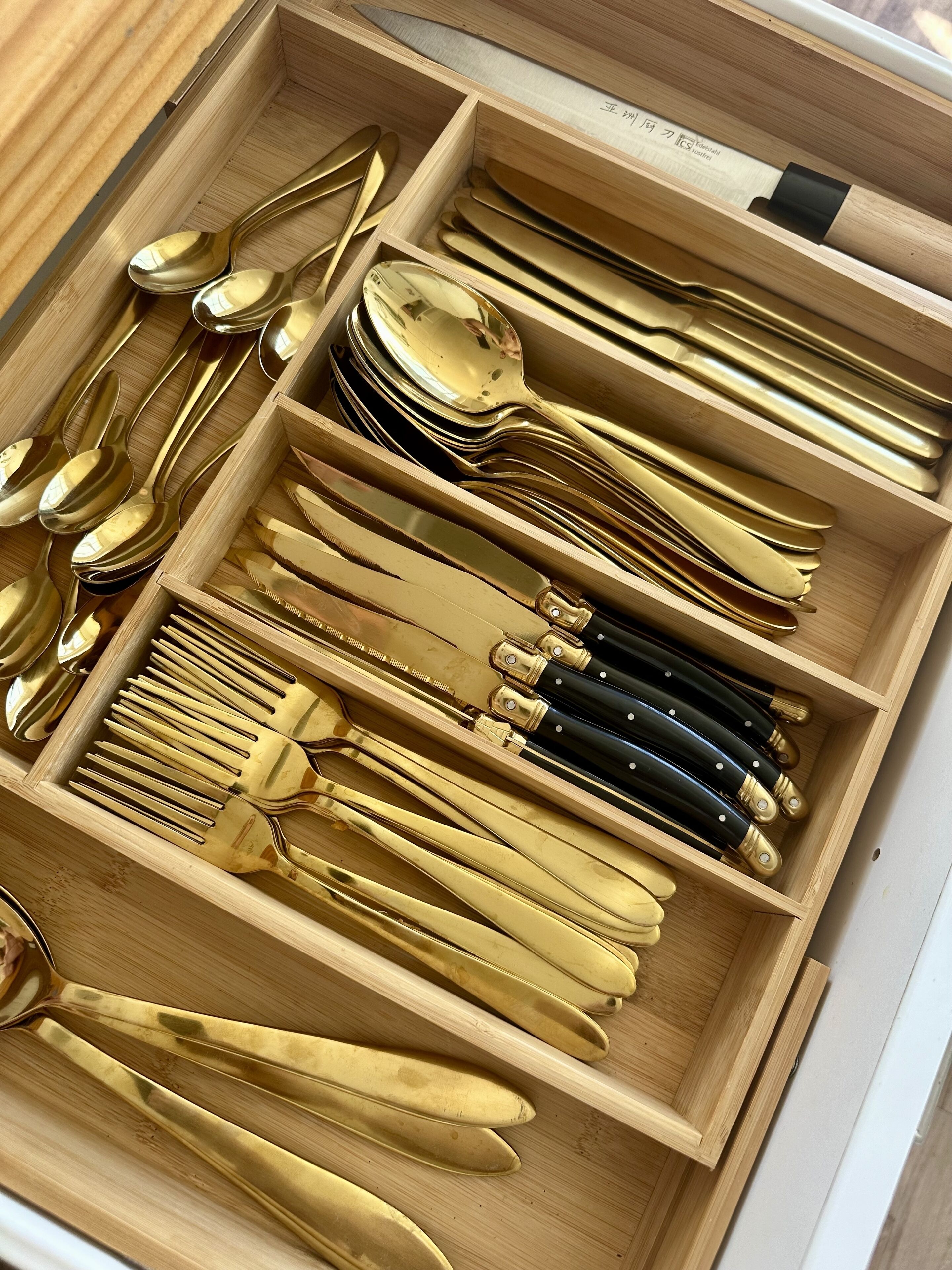 Un cajón con utensilios de cocina ordenados, incluyendo cucharas, tenedores, cuchillos y un rallador.