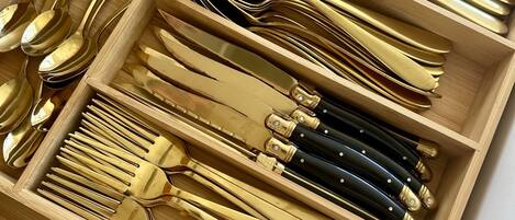 Un cajón con utensilios de cocina ordenados, incluyendo cucharas, tenedores, cuchillos y un rallador.