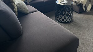 A modern living room with a sectional sofa, a round coffee table, and large windows offering a view of the outside.