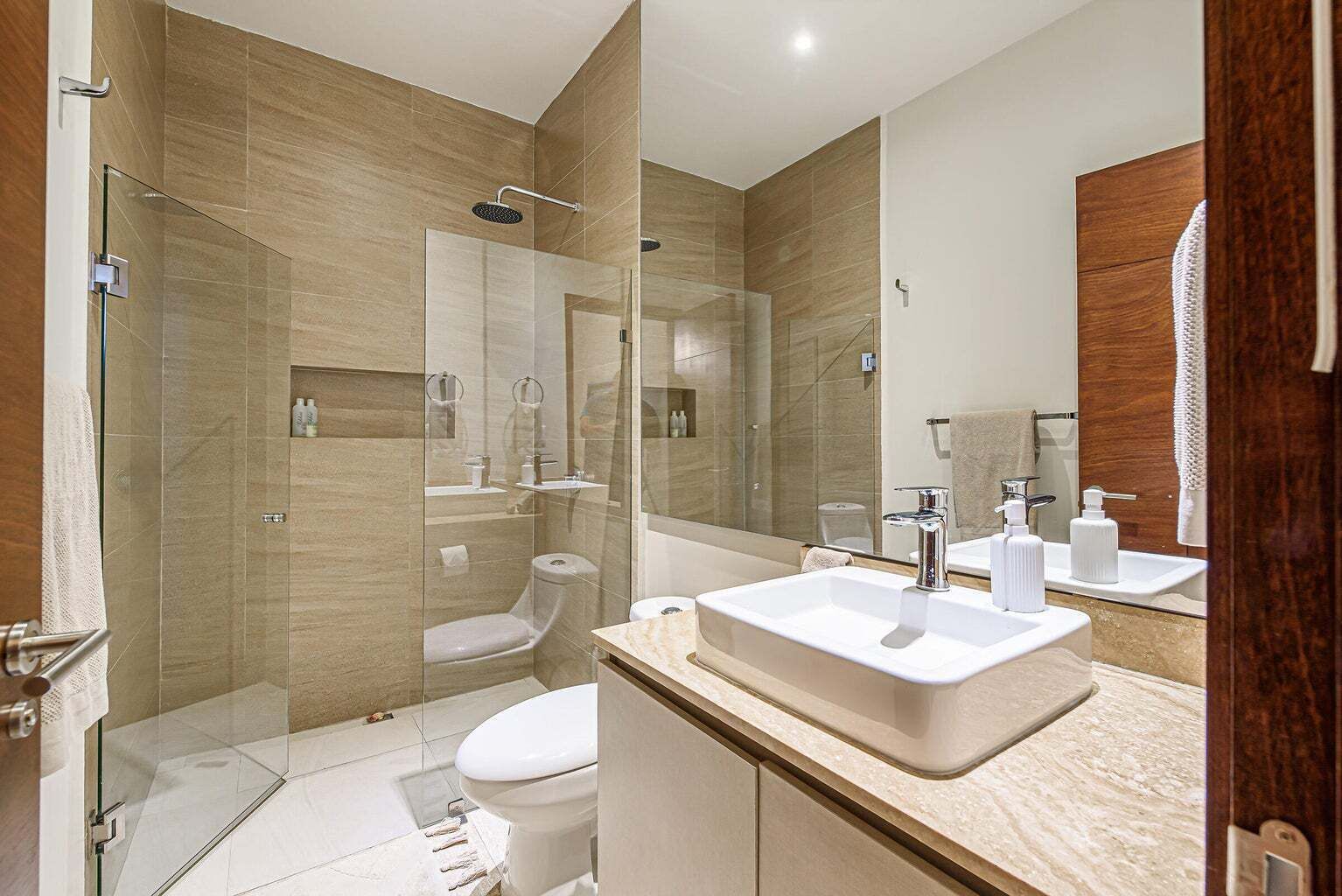 Un baño moderno con ducha de vidrio, inodoro blanco y tocador con un espejo grande.