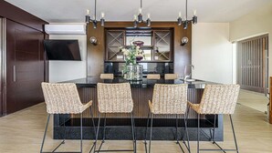 Una cocina moderna con una isla central, cuatro sillas de mimbre, un jarrón grande con flores e iluminación colgante.