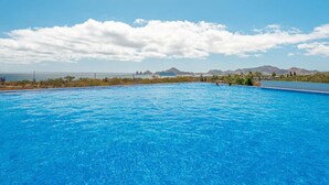 Una piscina grande y cristalina de color azul, con vistas a montañas y al océano al fondo.