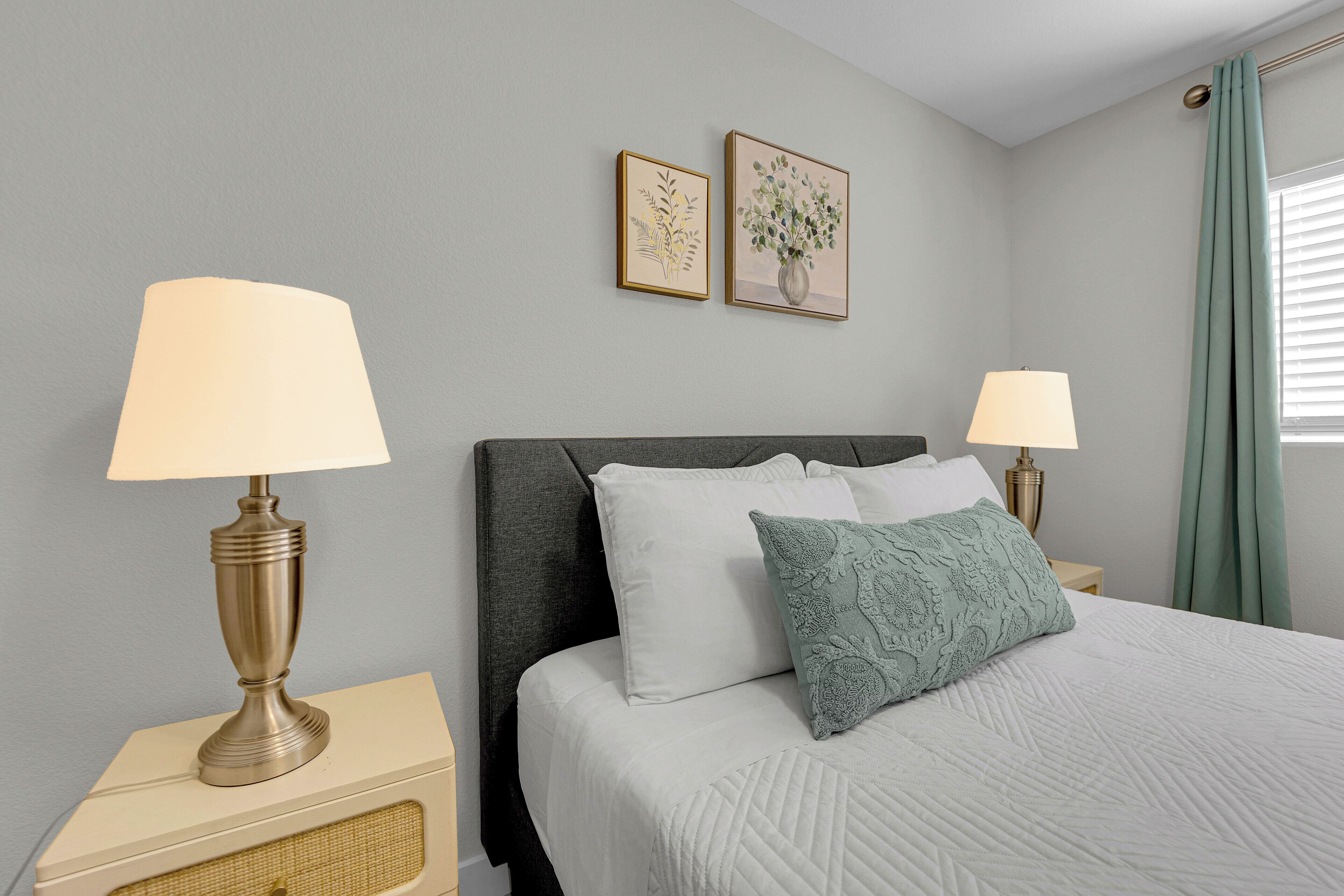 A neatly made bed with white bedding and a green pillow, flanked by two bedside lamps on nightstands.