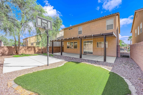 Um edifício residencial com uma cesta de basquete, um pátio coberto e um gramado bem cuidado.