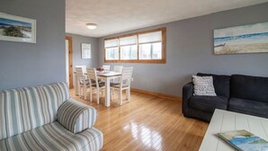 Ein Wohnzimmer mit einem gestreiften Sofa, einem dunklen Sofa, einem Essbereich mit Tisch und Stühlen sowie einem großen Fenster mit Blick.