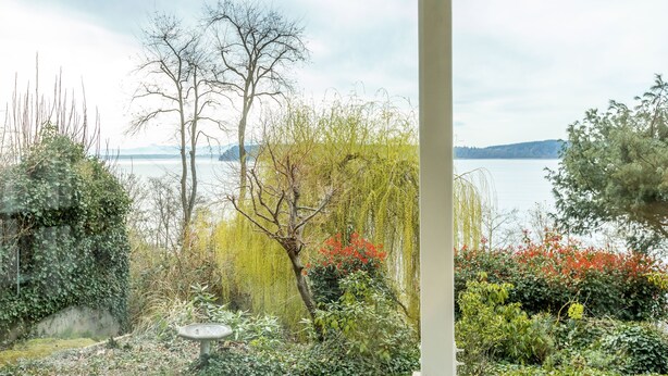 Un jardin où l’on trouve différentes espèces de plantes et un abreuvoir à oiseaux, offrant une vue sur un plan d’eau et des montagnes lointaines.